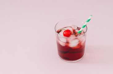 Cherry juice cocktail with green and white paper drinking straw, ice cubes and cherry fruit on pastel pink background. Minimal summer drink concept. Trendy summertime party idea. Summer aesthetic.