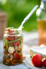 Delicious fresh salad with mozzarella and rocket in a glass for a picnic. Beautifully arranged antipasto for a healthy and tasty meal to take away. Vertical close-up with short depth of field.