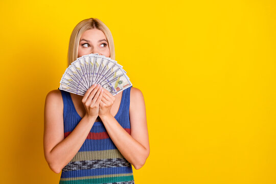 Portrait of shopaholic young blond lady in singlet holding her monthly payment credit money hiding face isolated on yellow color background