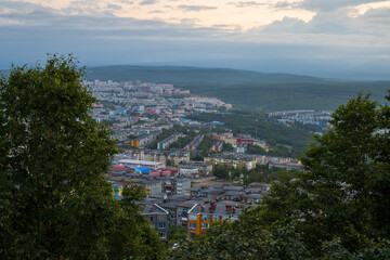 Morning cityscape. Top view of buildings and streets. Trees in the foreground. Cloudy weather. City of Petropavlovsk-Kamchatsky, Kamchatka Krai, Far East of Russia.