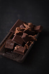 Pieces of dark chocolate on black background. Dessert food background.