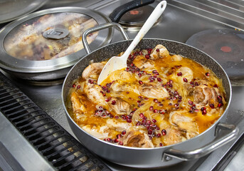 Pans with chicken meat and pomegranate stand on the stove, frying chicken, cooking, real picture in the kitchen