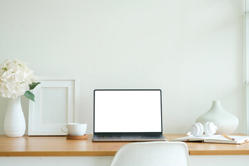 Front view laptop with blank white screen, books, coffee cup and picture frame on wooden table.