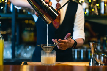 Professional male bartender preparing and serving cocktail drink to customer on bar counter at luxury nightclub. Barman making mixed alcoholic drink for celebrating holiday party at restaurant bar.
