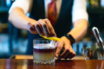Professional male bartender preparing and serving cocktail drink to customer on bar counter at luxury nightclub. Barman making mixed alcoholic drink for celebrating holiday party at restaurant bar.