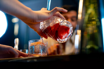 Professional male bartender preparing and serving cocktail drink to customer on bar counter at luxury nightclub. Barman making mixed alcoholic drink for celebrating holiday party at restaurant bar.