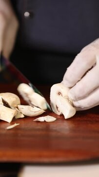 Close up view of male hands chopping  mushroom on wooden cutting board with knife
