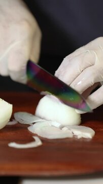 Close up view of male hands chopping  onion on wooden cutting board with knife