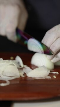 Close up view of male hands chopping  onion on wooden cutting board with knife