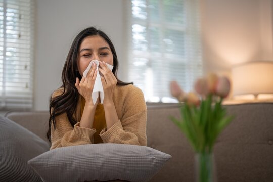 Woman sneezing due to pollen allergy at home. Concept of seasonal allergies