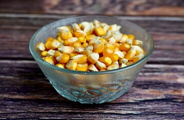 Dry yellow corns in glass bowl food ingredients photography isolated on horizontal ratio wooden table surface background.
