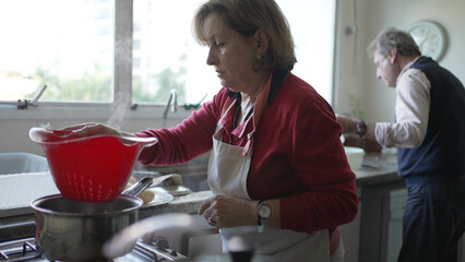 Elderly Woman Cooking with Husband in the Background in Their Home Kitchen