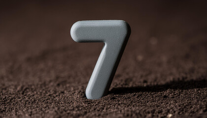 Number 7 made of gray stone isolated with shadow over dark sand.