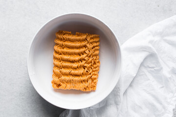Overhead view of spicy ramen noodles in a white bowl, top view of orange spicy noodles on countertop