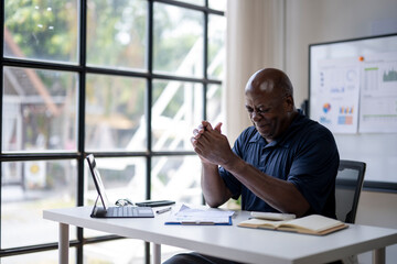 A man is sitting at a desk with a laptop and a stack of papers