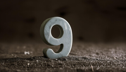 Number 9 made of gray stone isolated with shadow over dark sand.