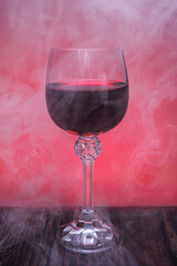 A beautiful glass of red wine surrounded by smoke. Glass with wine on a wooden surface.