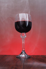 A beautiful glass of red wine surrounded by smoke. Glass with wine on a wooden surface.