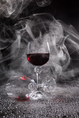 Two glasses on a black background. Smoke around a glass of wine. A glass of red wine stands on the surface, an empty glass lies next to it.