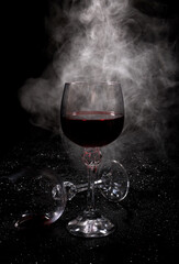 Two glasses on a black background. Smoke around a glass of wine. A glass of red wine stands on the surface, an empty glass lies next to it.