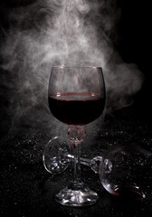 Smoke around a glass of wine. A glass of red wine stands on the surface, an empty glass lies next to it.