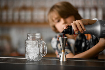 Little boy prepares a fruit cocktail with ice. He pours brown syrup into the jigger from the bottle