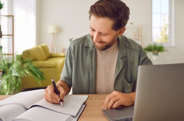 Positive man, a student, engages in online distance learning or work from home, sitting at a table...