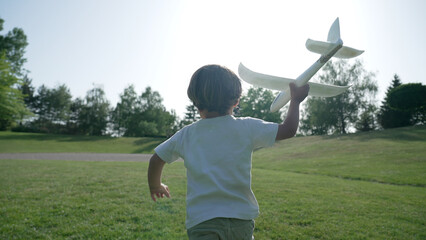 Little Boy Holding a Foam Airplane, Ready to Launch it Against a Clear Blue Sky in a Lush Park