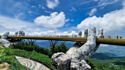 A bridge over a river is supported by a statue of a hand in a natural setting Vietnam Da Nang Ba Na...
