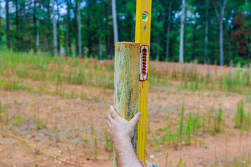 Man building wooden fence in backyard checking posts with level