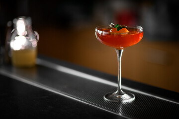 Stemmed glass filled with red brown cocktail garnished with citrus fruits and green leaves