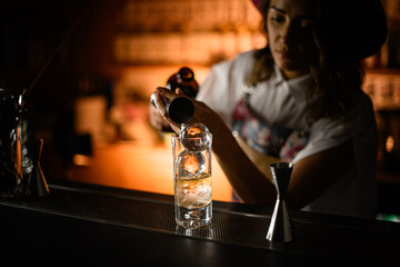 Female bartender pours a drink from a jigger into a tall glass