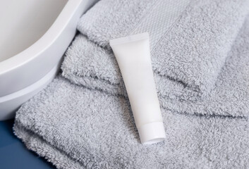 White cosmetic tube on grey folded towel near vessel basin close up in bathroom, mockup