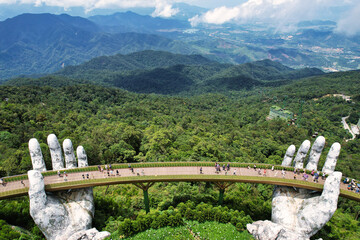 Statue of hands holding a bridge over a forest, towering over landscape Vietnam Da Nang Ba Na Hills...