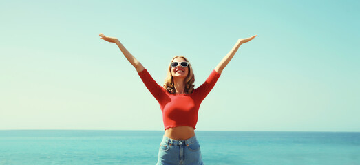 Obraz premium Summer vacation, happy inspired young woman raising her hands up on the beach on sea and blue sky