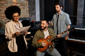 A music band rehearsing in a recording studio, with a group of people focused on playing an acoustic guitar.