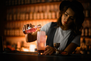 Female bartender is preparing a cocktail, pouring a pink drink