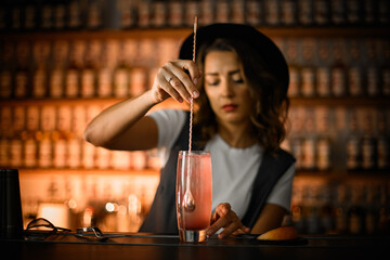 Female bartender stirs a pink cocktail with a long spoon