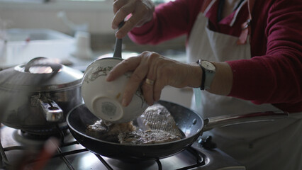 Senior Woman Cooking Fish in Kitchen - Authentic Home Cooking Scene