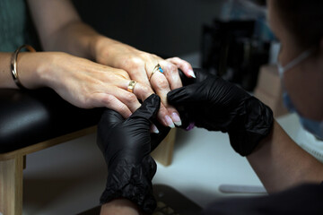 A manicurist in black gloves carefully working on a client’s nails, focusing on precision and...