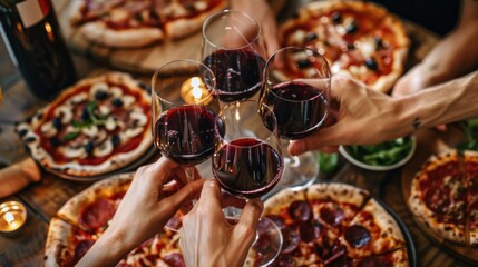 Friends eating pizza with wine, top view clinking glasses of red wine on pizza's simple wooden table.
