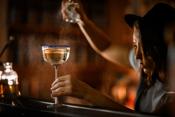 Glass with a tall metal stem and a blue rim sits on the bar, filled with a bubbly champagne-colored...