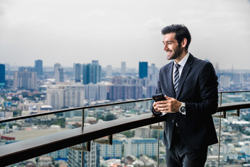 Smart and handsome businessman standing at balcony with cityscape background