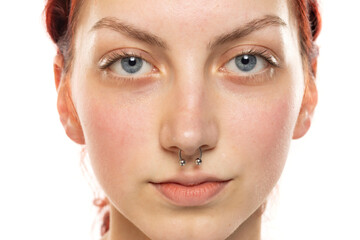 Portrait of a young serious woman without makeup, nose piercing and blue eyes on a white background