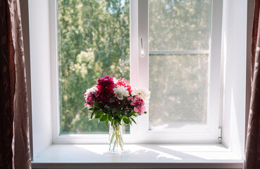 Beautiful peonies in a glass vase on the windowsill.