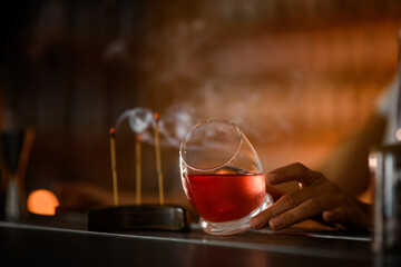 Female bartender rubs an unusually shaped tumbler with a convex bottom, filled with a pink cocktail