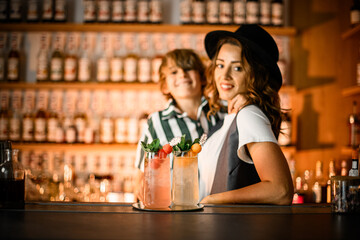 Woman bartender and little smiling boy standing near bar counter with tall glasses of cocktails