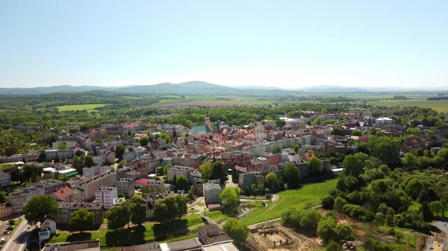 Historic town buildings and lush countryside, framed by distant hills under a clear blue sky. Prudnik, Poland - Prudnik, Polska