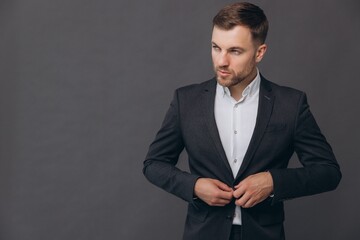 Caucasian millennial businessman isolated on gray studio background posing, satisfied successful man in formal suit buttoning up