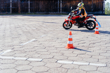 L-driver person drives slalom through the orange cones on motordrome on motorcycle